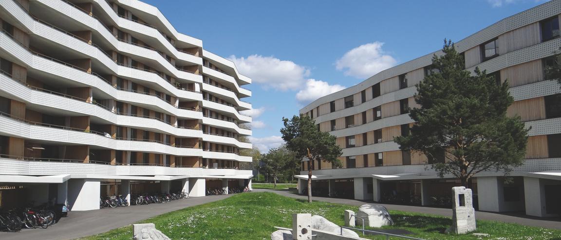 Zwei langgezogene mehrstöckige Wohngebäude des Zellwegerparks in Uster laufen von der Seite her aufeinander zu. Im Hintergrund in der Bildmitte bleibt ein schmaler Durchblick in die Umgebung.