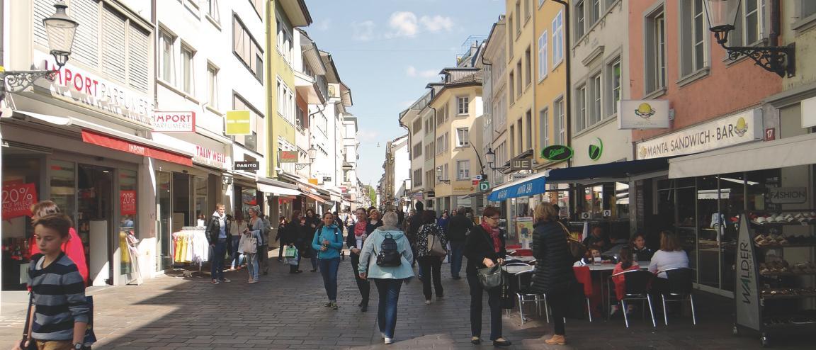 Blick in eine von renovierten Häusern gesäumte Gasse der Winterthurer Altstadt. Zahlreiche Passanten bummeln durch die Gasse, stehen vor den Läden oder sitzen an den Tischen eines Imbissstandes.