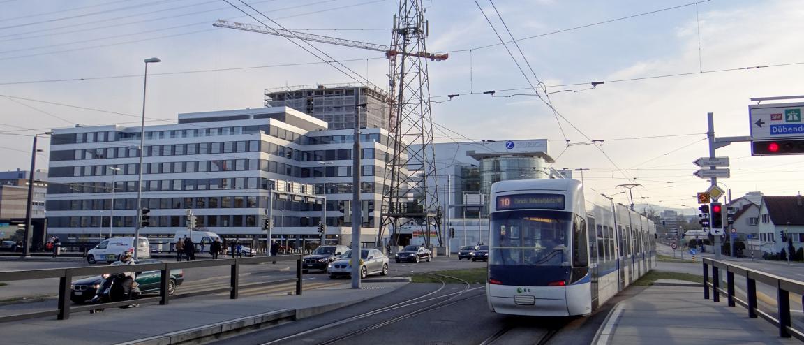 Ein Cobratram der Linie 10 verlässt die Haltestelle Glattpark stadteinwärts. In der Bildmitte stehen verschiedene Verwaltungsgebäude, nach links biegt im Vordergrund die Glattparkstrasse Richtung Fernsehstudio ab.