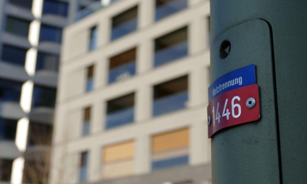 Ein Mast einer Strassenbeleuchtung mit einer Wohnsiedlung im Hintergrund